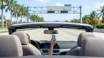 Driver in a car rental passing under a SunPass toll sign on a sunny Miami highway