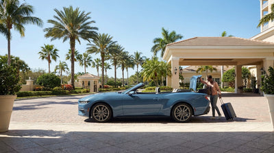 A modern rental car driving on a coastal road lined with palm trees on a sunny day in Florida