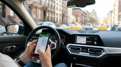 A driver uses a smartphone for directions in their car hire with a blurred view of New York City traffic ahead