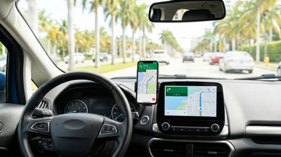 A driver using a smartphone for navigation in a car rental on a sunny, palm-lined street in Miami