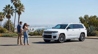 A white sedan car hire is parked safely on a scenic road overlooking the sunny Los Angeles skyline