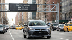 White car rental navigating heavy traffic on a congested New York street with tall skyscrapers in the background