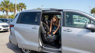 A parent secures a child in a car seat inside their car hire vehicle on a sunny Florida road