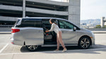 A parent installs a child car seat in the back of a car rental at a San Francisco airport parking garage