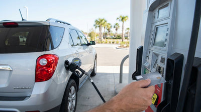 A person refuels their car rental at a gas station pump under the bright sun in Texas