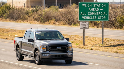 A pickup truck from a car rental service drives on a Texas highway toward a weigh station sign