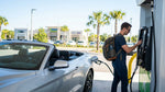 A driver refueling their white car hire sedan at a gas station with palm trees in sunny Orlando