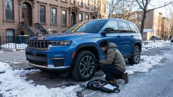 A white car rental equipped with snow chains driving on a snowy road in New York