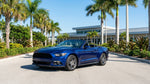 White convertible car hire driving along a sunny coastal highway lined with palm trees in Florida