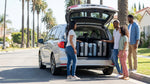 Four adults loading suitcases into a large SUV car rental on a sunny street in Los Angeles