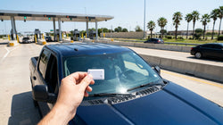 White car rental vehicle driving under an overhead electronic toll gantry on a Texas highway
