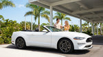 A young driver smiling in their convertible car rental with Miami's sunny beaches in the background