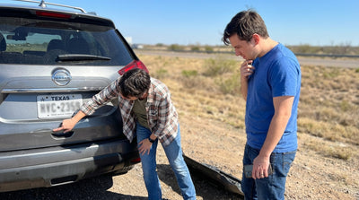 A driver inspects a minor scrape on their car rental on the side of a sunny road in Texas