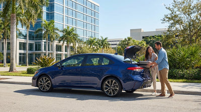 A person stands by their silver car hire vehicle on a sunny downtown street in Orlando