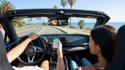 A smartphone with a map mounted to the dashboard of a car rental on a scenic highway in California