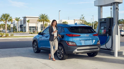A person pumps gas into a silver car rental at a sunny gas station with palm trees in Miami