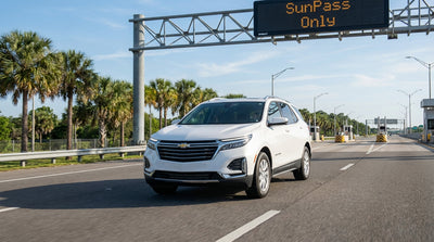 A white car hire approaches a SunPass Only toll gantry on a sunny highway in Florida