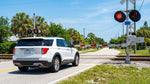 A white car hire stopped at a railroad crossing with flashing red lights on a sunny day in Florida