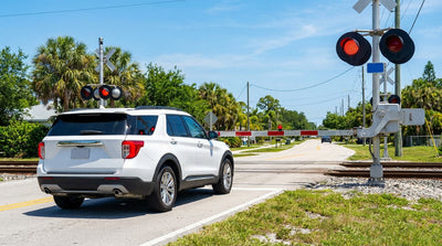 A white car hire stopped at a railroad crossing with flashing red lights on a sunny day in Florida