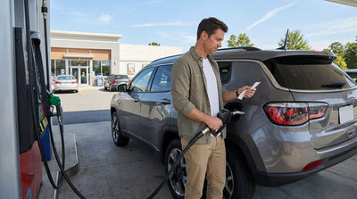 A person refueling a silver car rental at a gas pump at a service plaza in Pennsylvania
