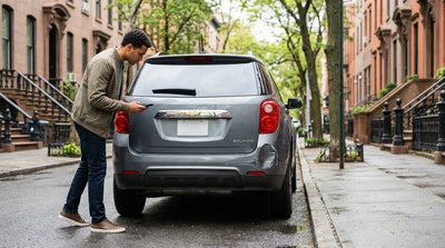 A parked car hire on a New York street with a large dent and scrapes on its rear bumper