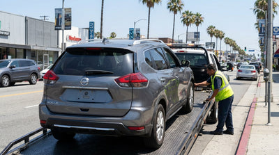 A tow truck hooking up a modern car hire on a sunny, palm-lined street in Los Angeles