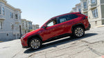 A red rental car driving up a steep hill lined with Victorian homes in San Francisco.
