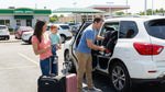 Parents installing a child seat in a white rental SUV outdoors, preparing for a family road trip with a toddler.