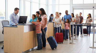 A family with luggage waits in line at a busy, well-lit car rental agency counter, indicating high demand.