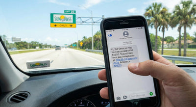 Phone displaying a scam toll text message inside a Florida car hire near a SunPass sign.