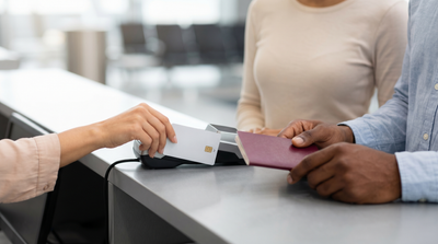 Hands place a foreign credit card on a counter terminal with a passport for car rental in New York.