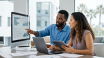 A diverse couple compares complex data on multiple screens in a bright modern Los Angeles office before booking car hire.