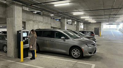 Woman paying at a parking kiosk next to a grey Chrysler Pacifica car hire in a Manhattan garage.