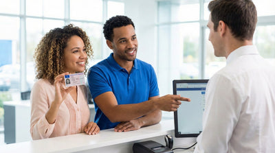 A happy couple is at a car rental desk in a bright office, showing their new driving licence to a friendly male agent.
