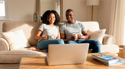 Couple sitting on a sofa using a laptop to book a rental car online from home.