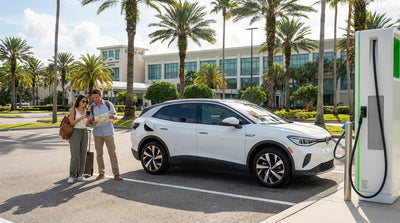 A white electric SUV car hire plugged into a charging station in a sunny Orlando parking lot with palm trees