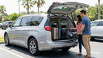 A silver Chrysler Pacifica minivan with its large trunk open, being loaded with two large suitcases and a pram in an Orlando parking lot.