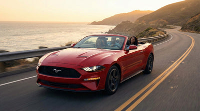 People enjoying a sunset drive on the Pacific Coast Highway in a red Ford Mustang convertible rental car with ocean views.
