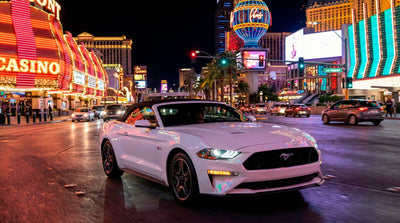 White Mustang convertible rental car driving along the Las Vegas Strip lights at night.