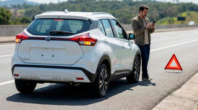 Driver calling for roadside assistance next to a white car rental with a flat tire and warning triangle.
