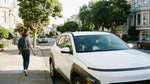 A woman walks away from a secured, empty white rental car parked on a San Francisco street.