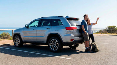 Couple stopping to sightsee near the coast with their silver Jeep Grand Cherokee rental car.