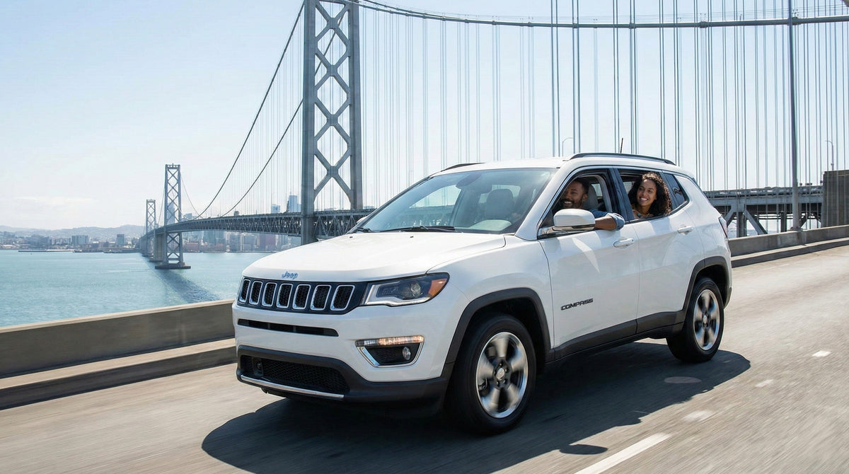 A couple smiling while driving a white Jeep Compass rental car across a major suspension bridge near San Francisco.