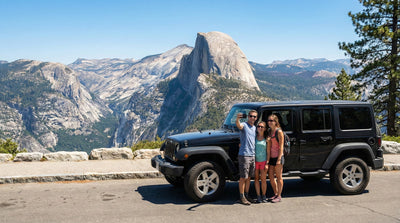 Friends taking a selfie next to a black Jeep Wrangler car hire during a sunny day trip to Yosemite.