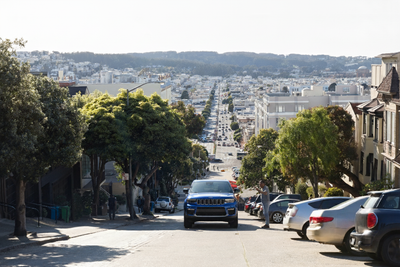 Modern SUV on a steep San Francisco street, with city skyline in background, perfect for car hire and car rental.