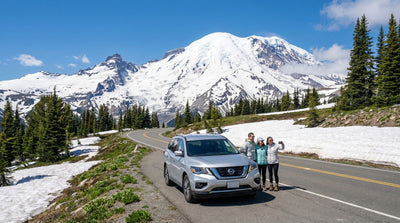 Family standing near a silver Nissan Pathfinder car rental with Mount Rainier snowy peaks in the background.