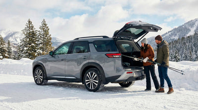 Couple loading ski gear into a rugged SUV car hire trunk for a winter trip in snowy mountains.