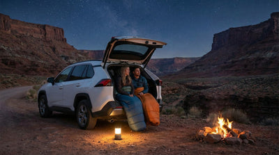 Travelers sleeping in the back of a rental car SUV under the stars during a camping road trip.