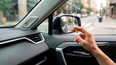 Hand holding a cigarette inside a vehicle, illustrating the strict no-smoking policy in most car rentals.