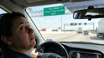 Worried driver looking at a green TxTag toll road sign while driving a Texas car hire vehicle.